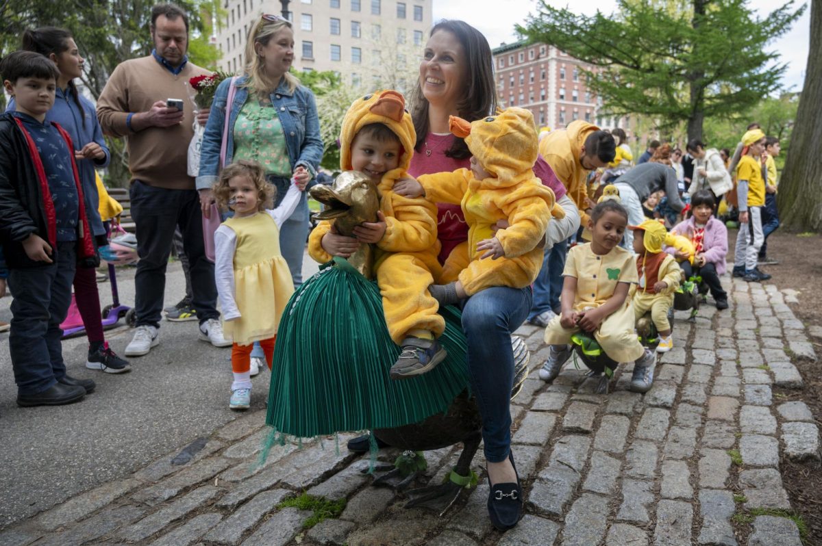 A mother holds her two ducklings while sitting on one of the duck sculptures for a photo. Children took turns sitting on the bronze ducks following the parade.
