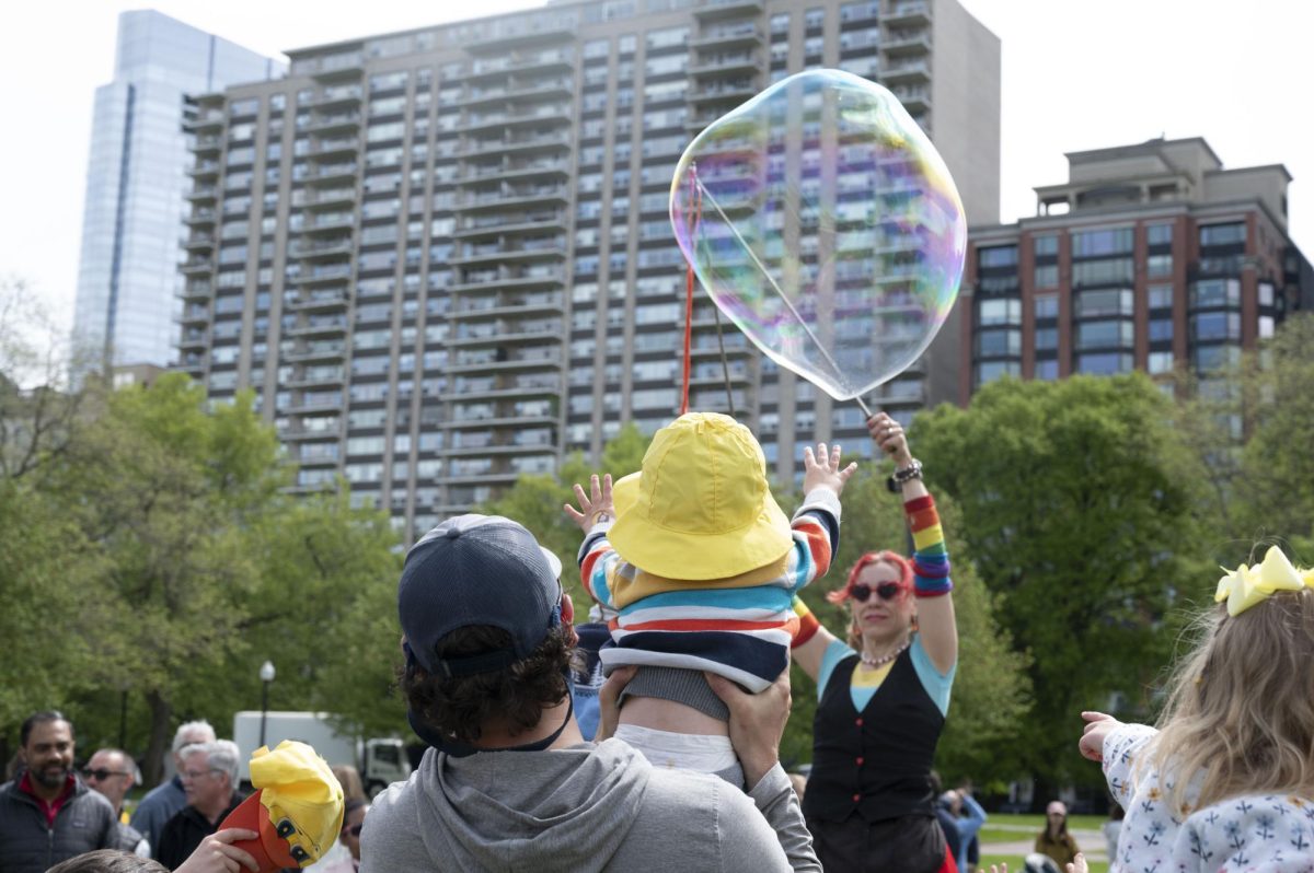 A father holds his child up as they reach for a large bubble. Many parents hoisted their children onto their shoulders so they could reach the bubbles.