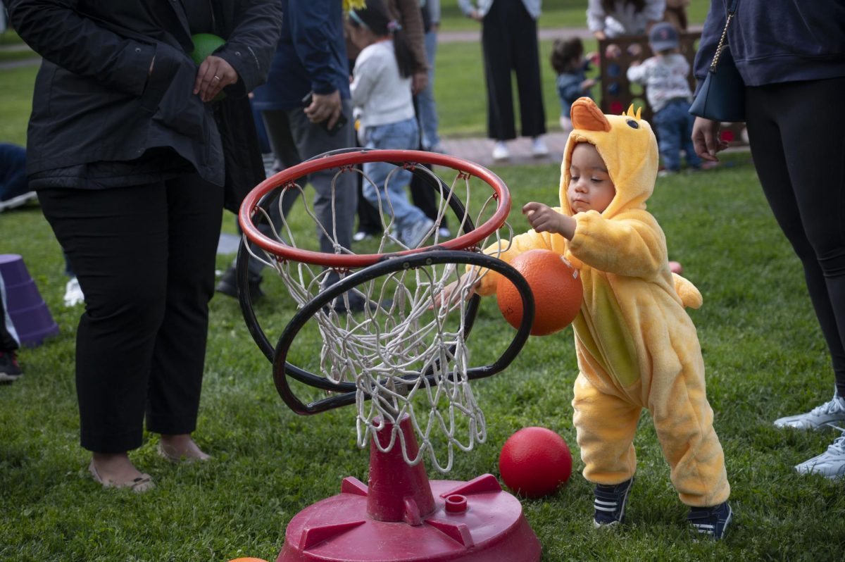 A child dressed in a duck onesie attempts to throw a ball into a basketball hoop. Other playground games included a parachute, tetherball and multiple Rody Max bounce horses.