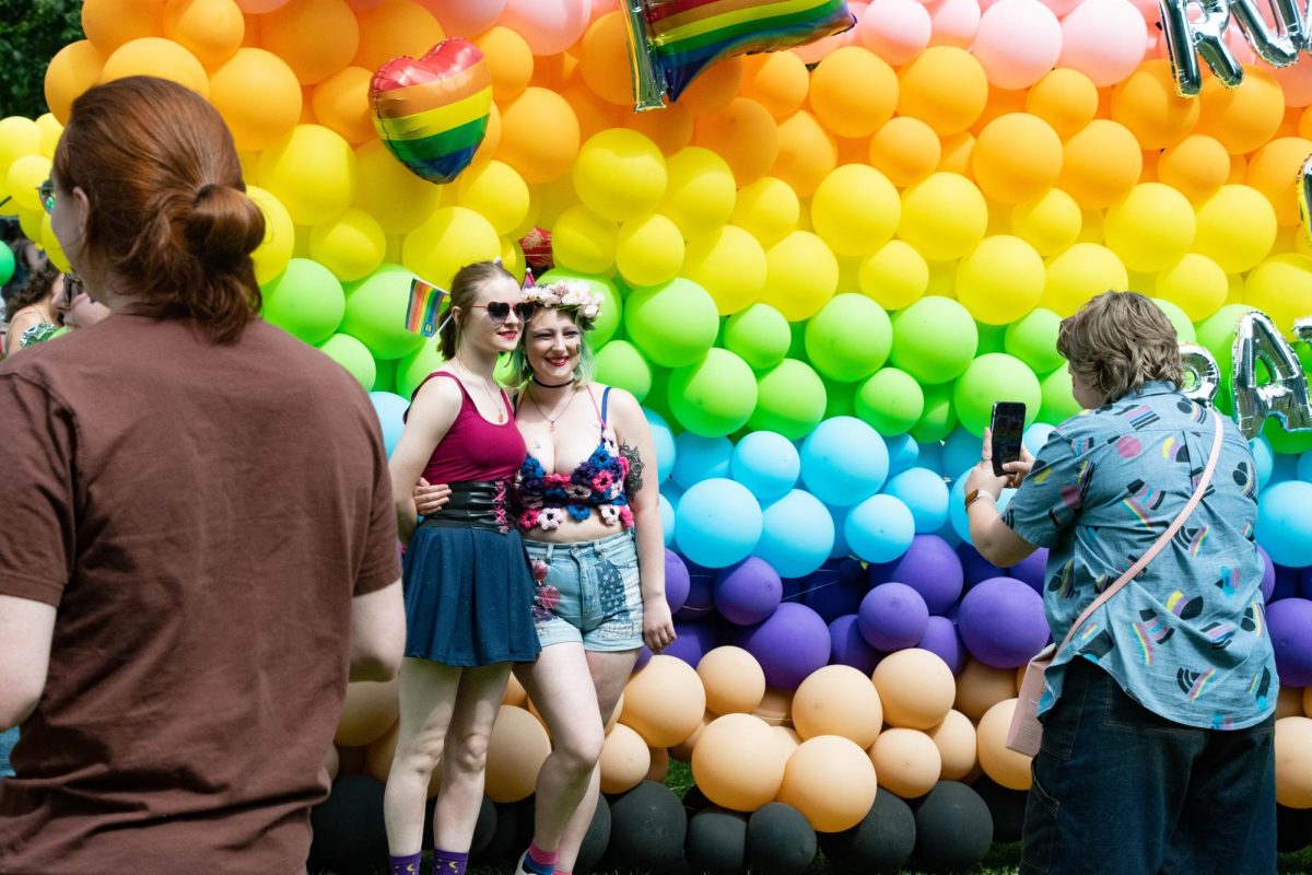 Two people pose in front of the Road of Rainbows balloon wall.