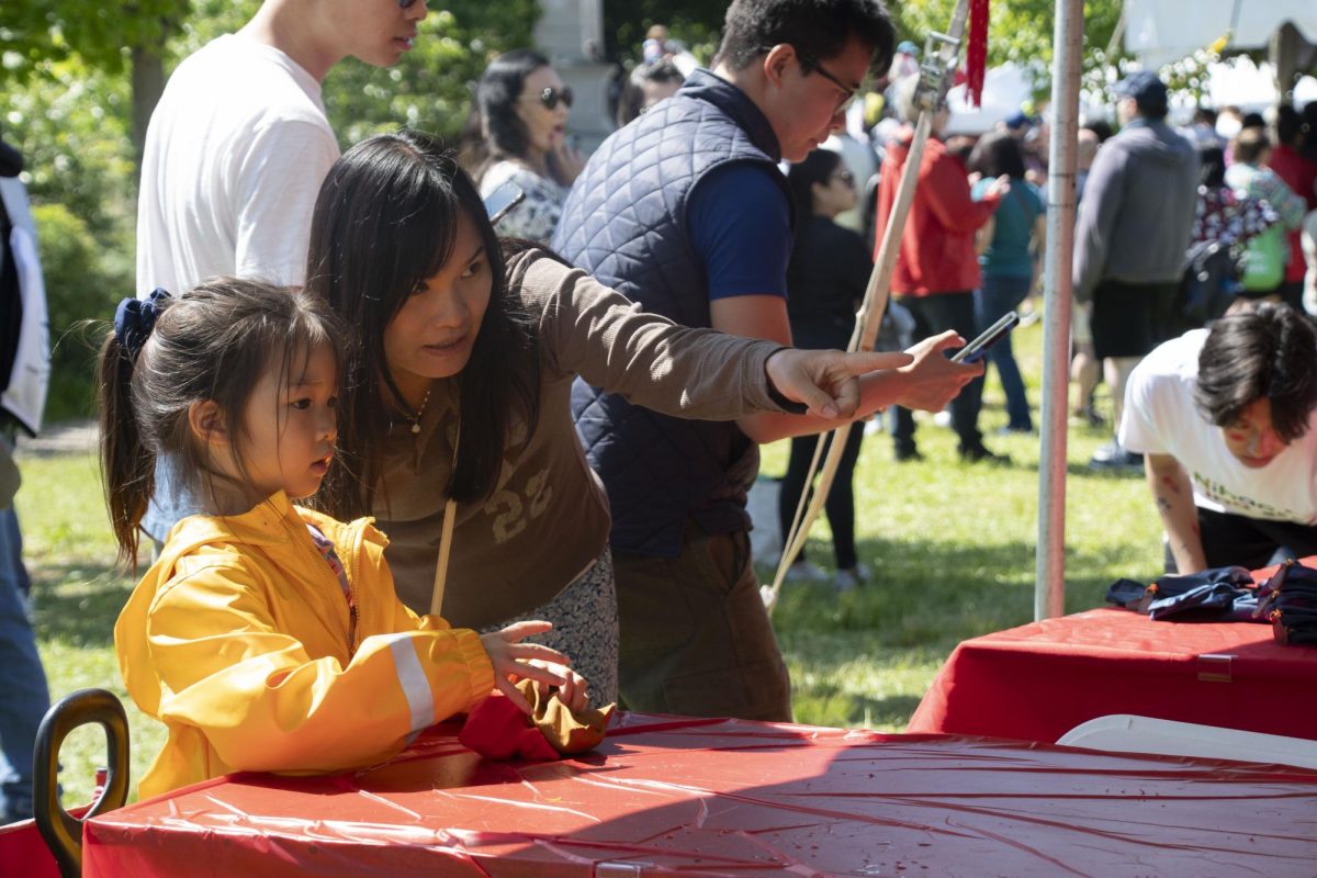 A mother points toward a tabletop cornhole game, directing her daughter toward where to aim the bean bags. The game was hosted by the Hong Kong Economic & Trade Office, which gave out items such as tote bags and water bottles depending on how many points participants scored.