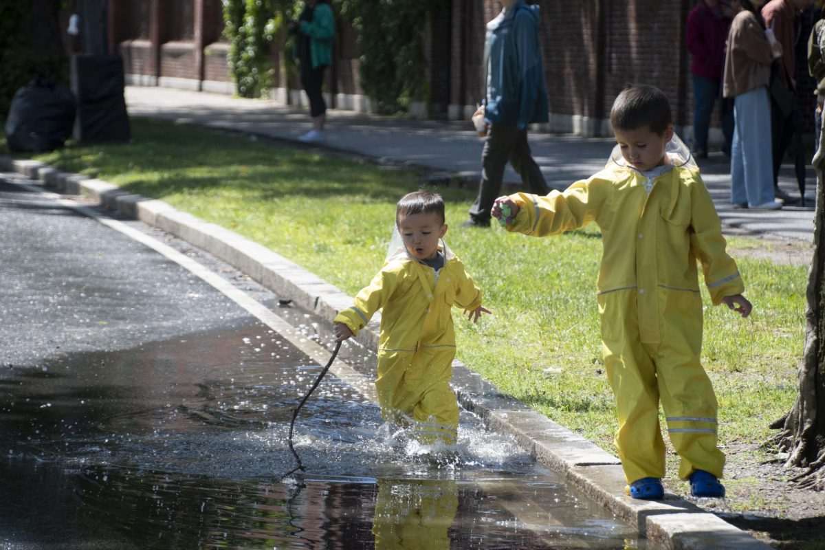 A child in a yellow raincoat runs through a puddle with a stick. The family-friendly event welcomed people of all ages.
