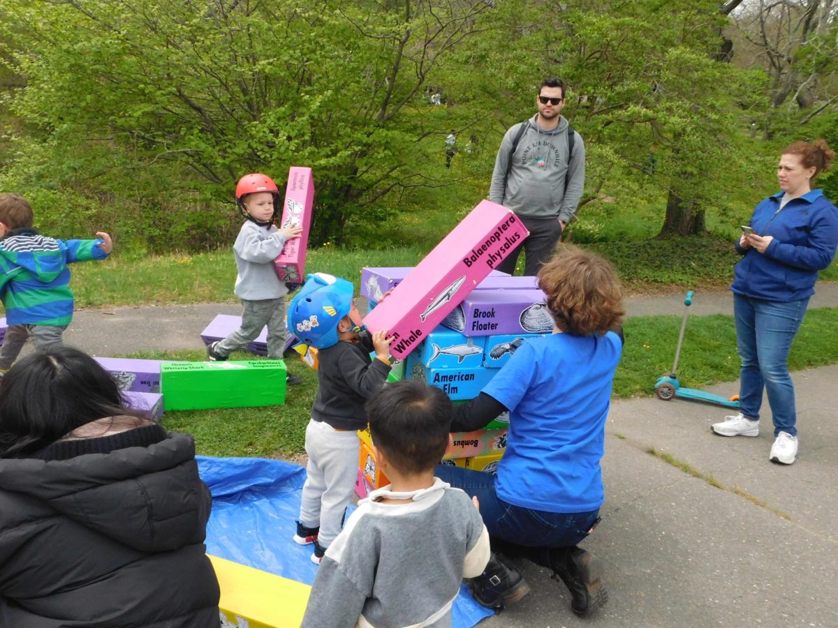 A group of children play a game of Jenga with giant, animal-themed blocks. The game aimed to teach children how the food web works and was made by Mothers Out Front, an organization of mothers that teaches people about climate change.