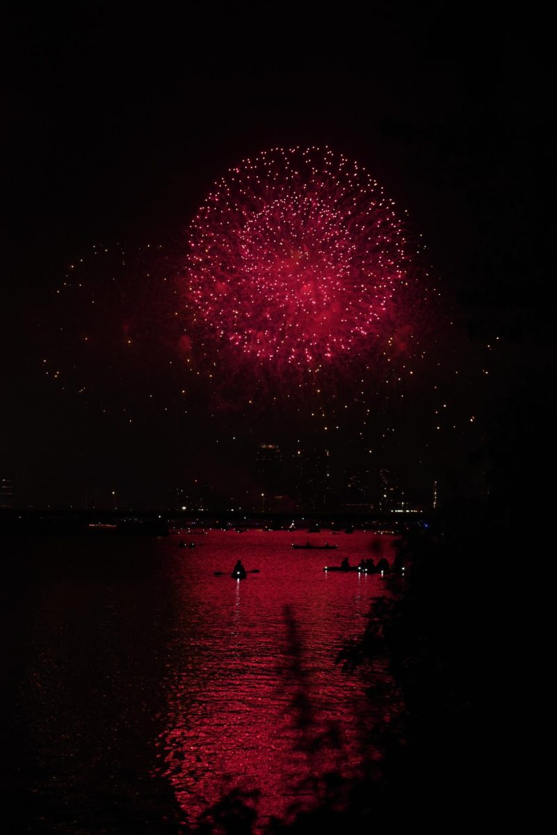 Kayakers observe the fireworks show from the Charles River. Red fireworks lit up the sky and shined across the Boston cityscape and the Harvard Bridge.