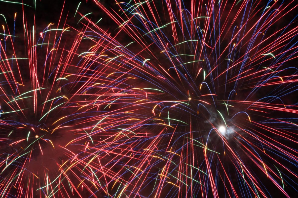 The individual colored streaks of a firework stream out from the bright white nucleus of the firework. Most spectators filmed or photographed the fireworks on smartphones.