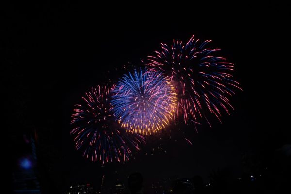 A blue firework tinged with gold glows overhead, flanked by two other fireworks whose streamers are burning out. Many fireworks were equipped with several stages that burned on different timeframes or with different hues.