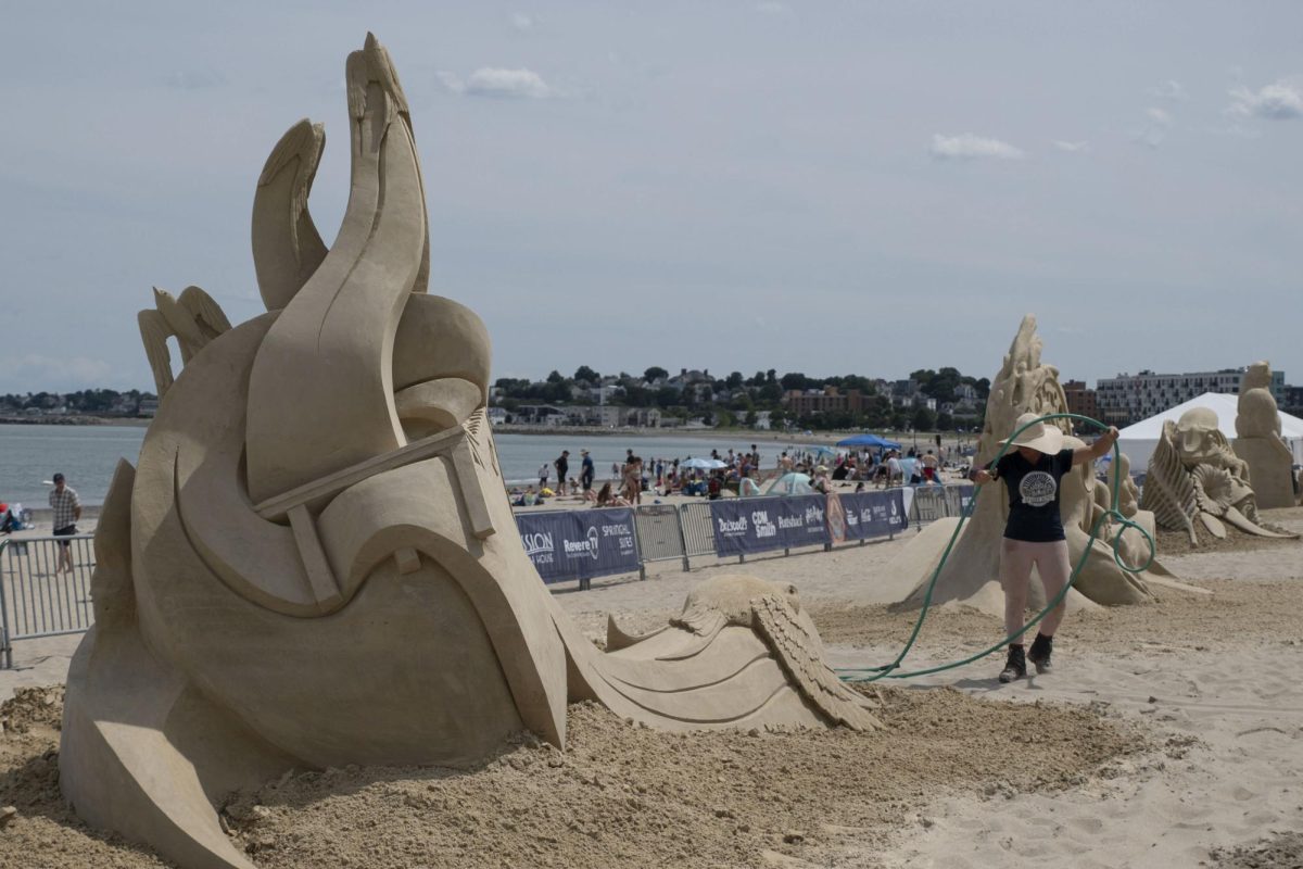 A professional sand sculptor drags a hose while standing next to a sand sculpture titled “Barn Swallow, Swallow, Barn.” The sculptures were made purely from sand and water.