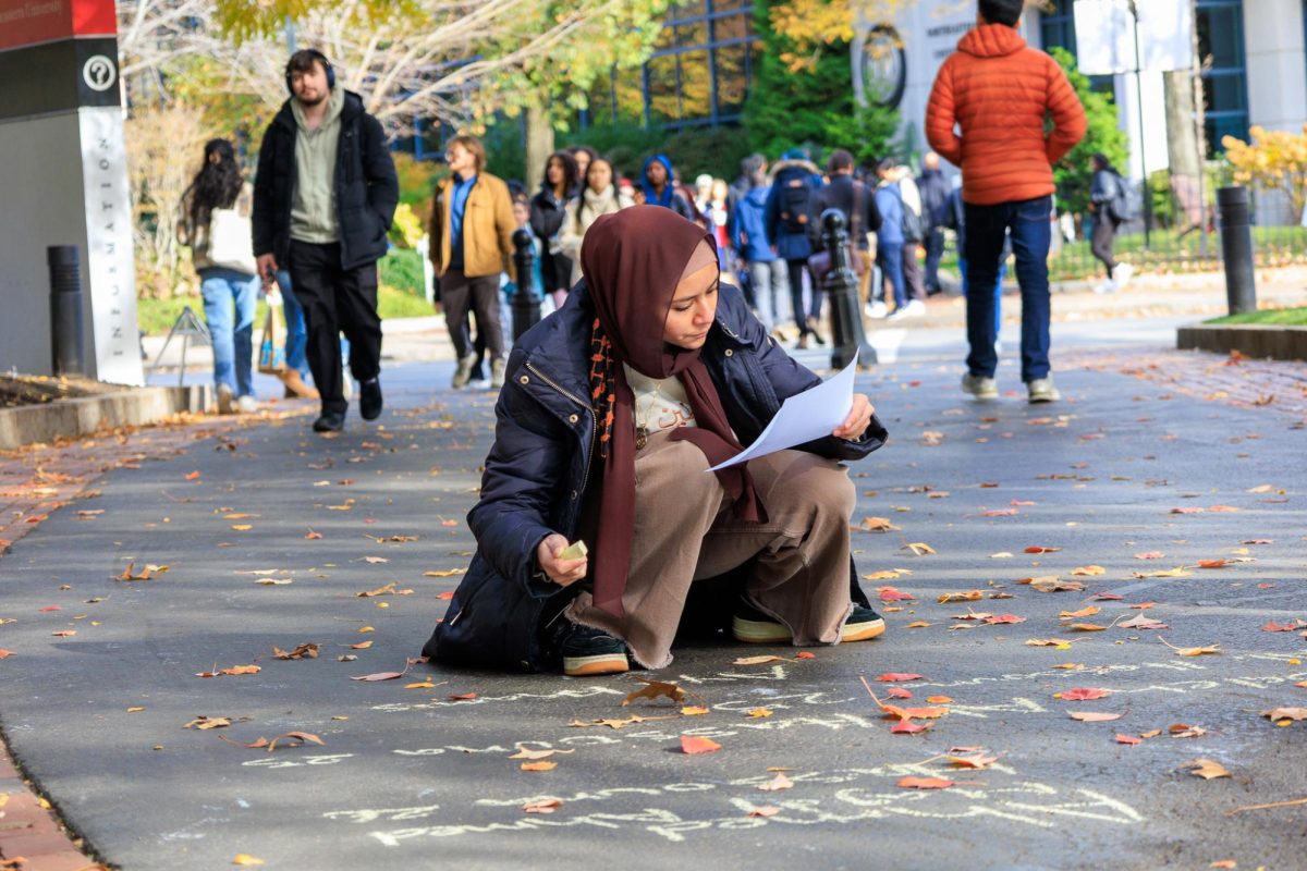 Mariam Hassan writes down the names of Palestinian victims of the Israel-Hamas conflict on the sidewalk surrounding Centennial Common during a chalk-in organized by NUSJP and NUSLSJP Nov. 15. Hassan authored the majority of the Title VI complaint and holds several leadership roles in both NUSJP and NUSLSJP.