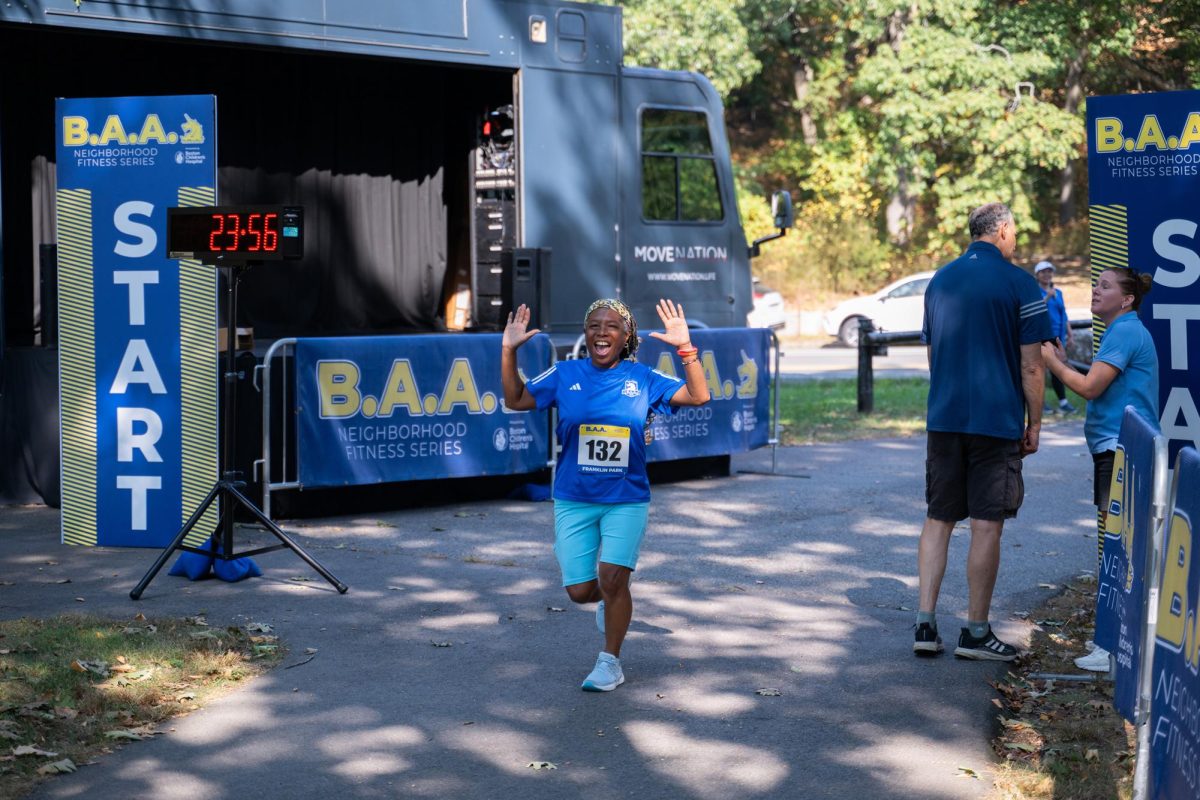 A woman raises her hands and smiles as she runs past the finish line.