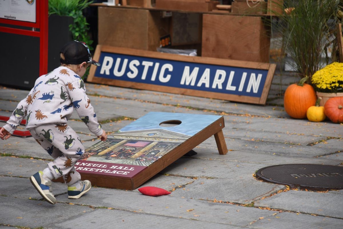 A young boy runs to collect a thrown bean bag while playing cornhole. Fall Fest offered a variety of activities and attractions, making it a perfect day for families to enjoy together.