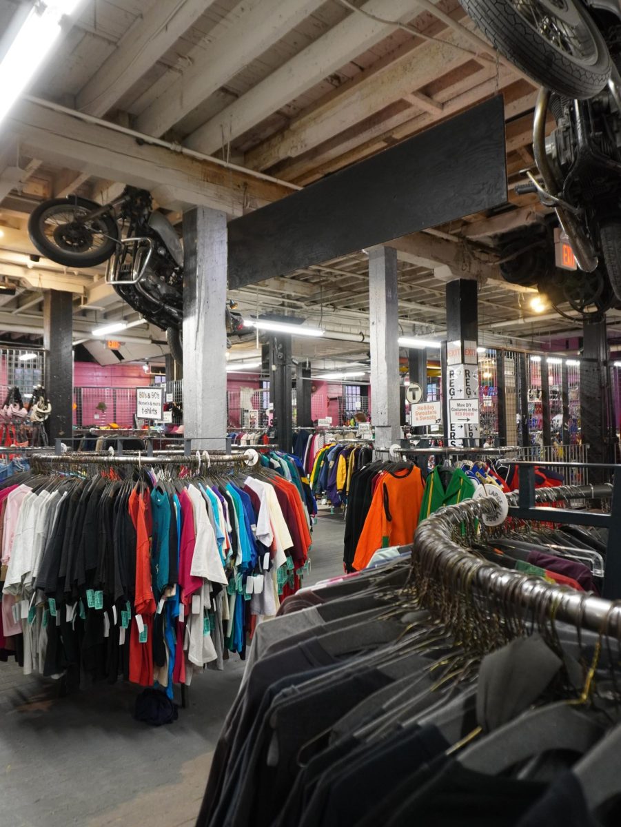 Old motorbikes hang above racks of clothing. The colored tags indicated differences in the age of clothing, ranging from recent to vintage.