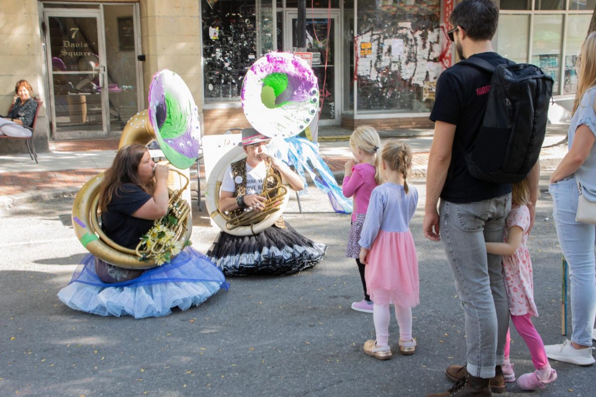 Two performers play their tubas while children and their parents look on. Some musicians wandered Davis Square on their own between band sets, talking to passersby and serenading small crowds.