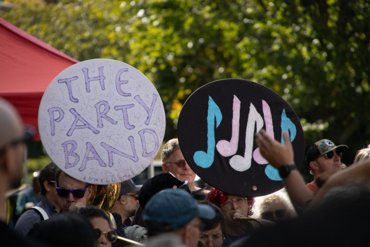 Musicians from The Party Band play for an enthusiastic crowd, with their band name and a stylized transgender flag painted on their tuba covers. Many bands used their instruments creatively to advertise themselves or advocate for a cause.