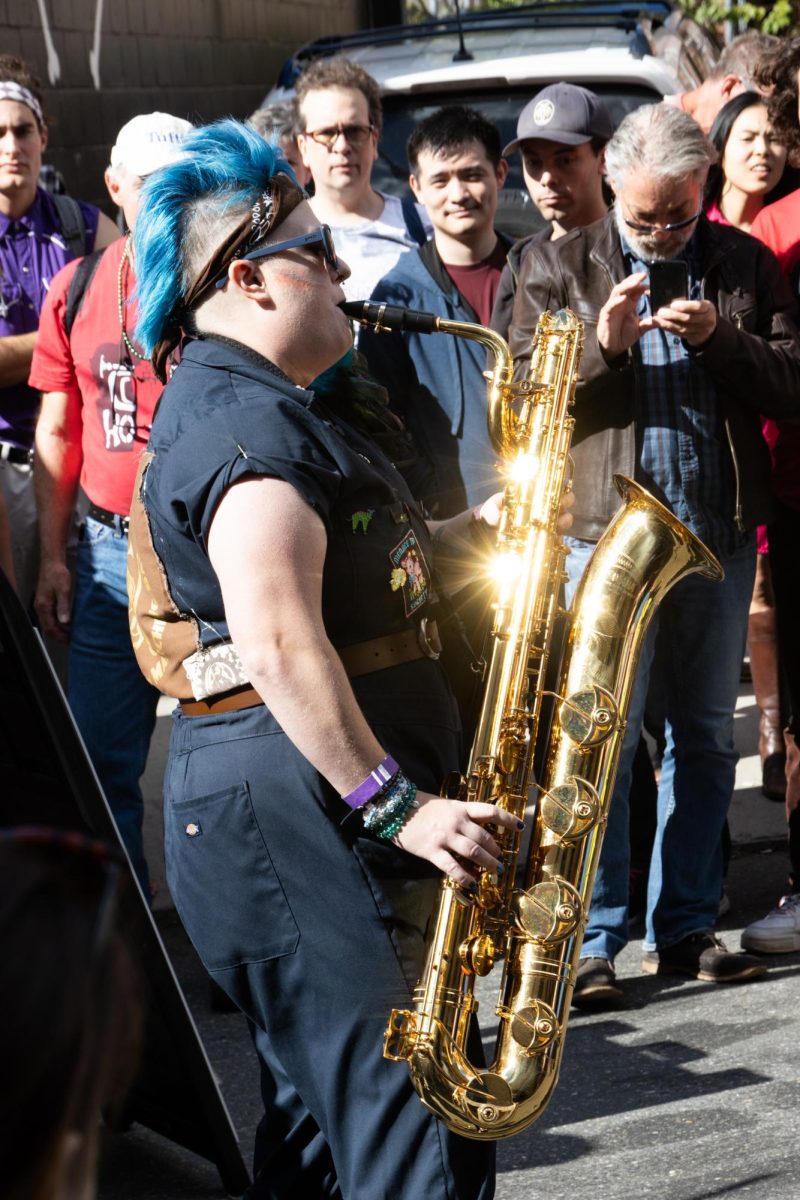 A bass saxophonist from Emperor Norton's Stationary Marching Band plays a solo, their instrument glinting in the sunlight. The weather cooperated with the festival, and the bright sunlight was welcomed by crowds after a week of spotty rainstorms.