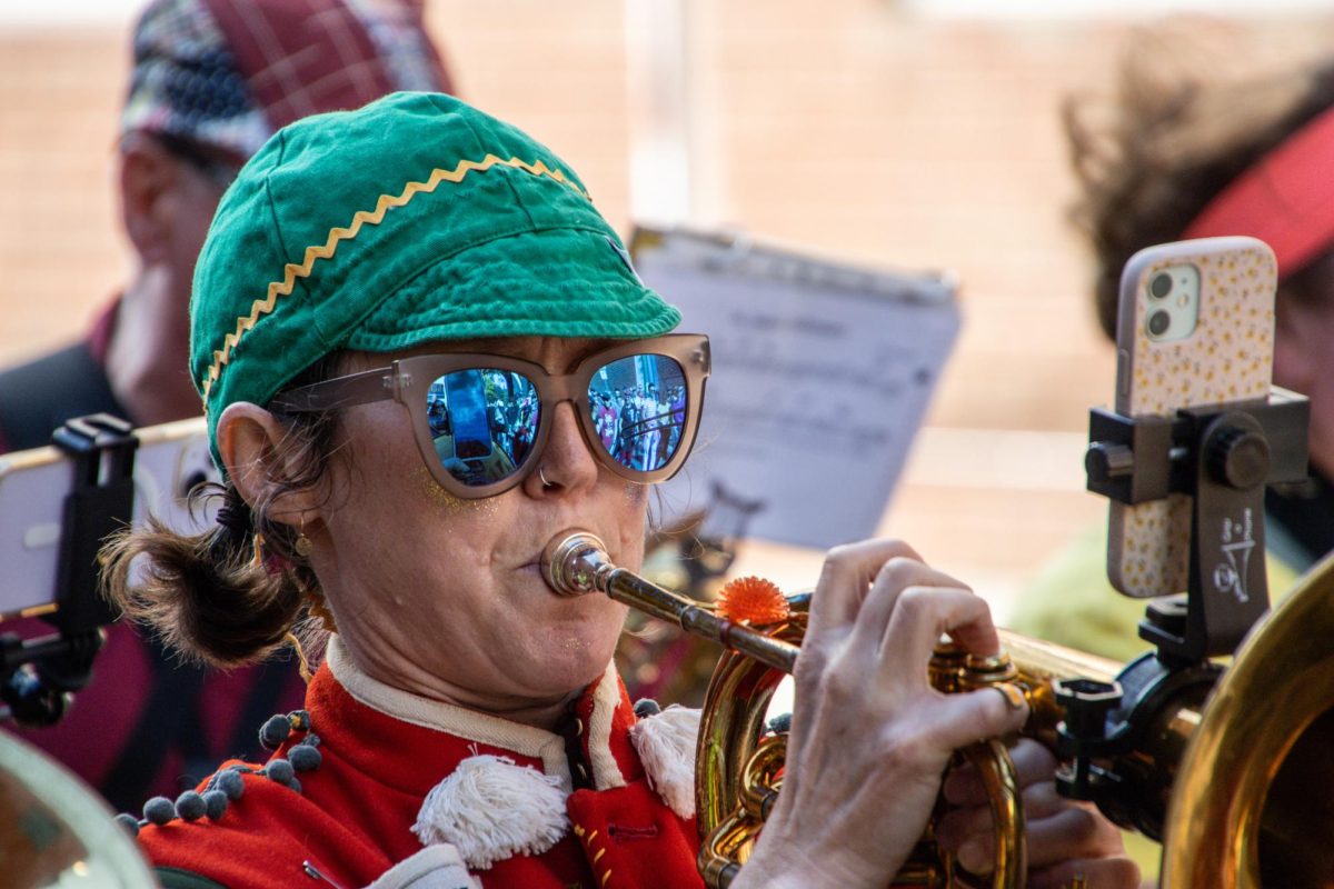 A trumpet player performs in sunglasses while reading sheet music from an iPhone mounted on their instrument. Performers attached stacks of sheet paper or their smartphones to their instruments while playing longer, more complex songs, but usually relied on their memory.