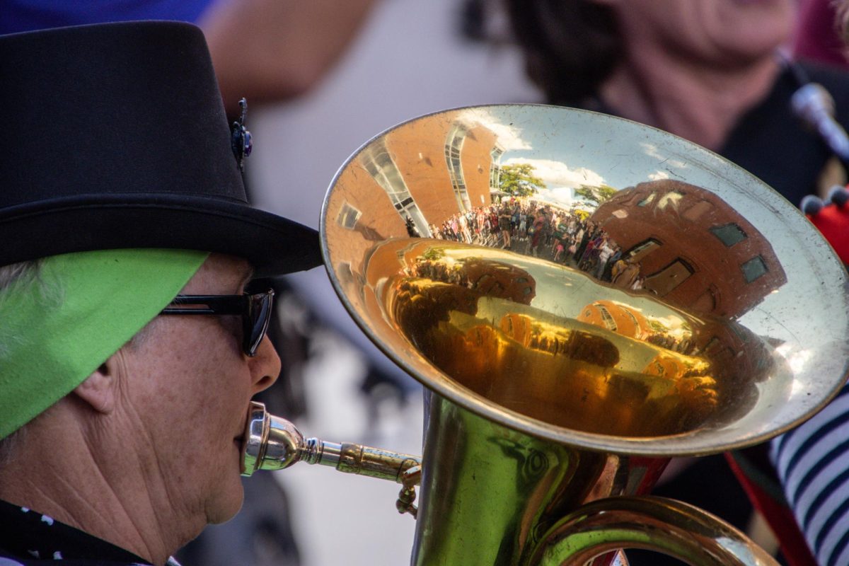 A tubist plays while the crowd around them is reflected in the brassy sheen of their instrument. Many performers polished their instruments to a mirror shine for the festival, while others used vintage instruments that had become tarnished with use.