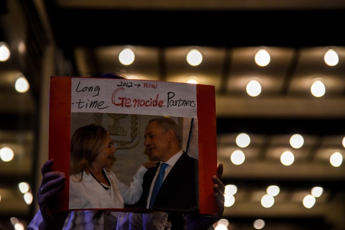 Underneath the lights of the Wang Theatre, a protester holds up a sign picturing Israeli Prime Minister Benjamin Netanyahu as patrons for Clinton’s event enter the theater. Some signs carried by protesters also contained imagery involving Clinton in the context of the current war occuring in the Middle East.