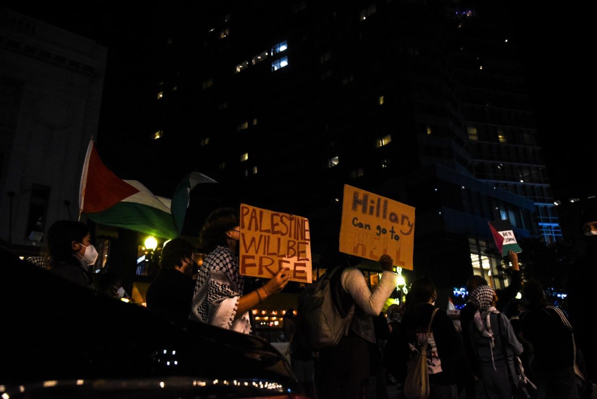 A line of protesters pass the front of the Wang Theatre holding signs. Many protesters wore masks to conceal their faces.