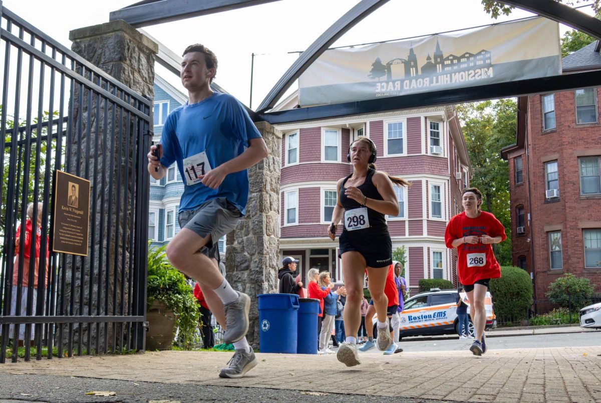 Three participants run through the Kevin W. Fitzgerald Park gate. The 5K aimed to raise funds and awareness for the housing crisis in Mission Hill.