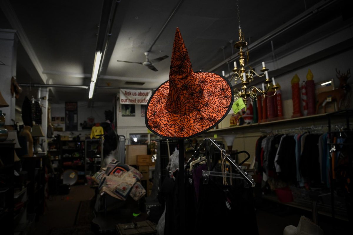 An orange witch hat adorned with black spiders and webs sits on a rack in the Witch City Consignment & Thrift shop. All kinds of Halloween-themed items were available for purchase, like ghost decorations and lights, with witch hats being a common item in many district shops.