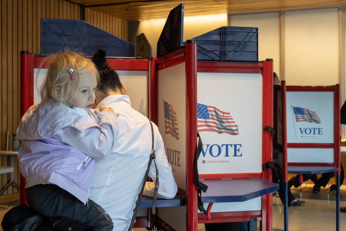 A mother rests her child on her hip while completing her ballot. The child excitedly received an “I Voted” sticker and showed it off to her family.