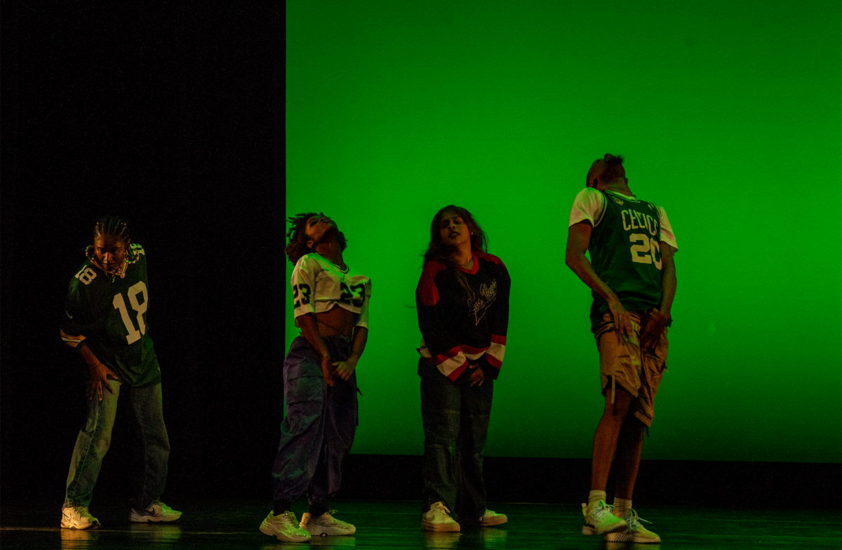 Northeastern’s Yung Mula performs in coordinating jerseys and baggy bottoms in front of a bright green background. Mischa Moxey, a fourth-year bioengineering major, led the group.