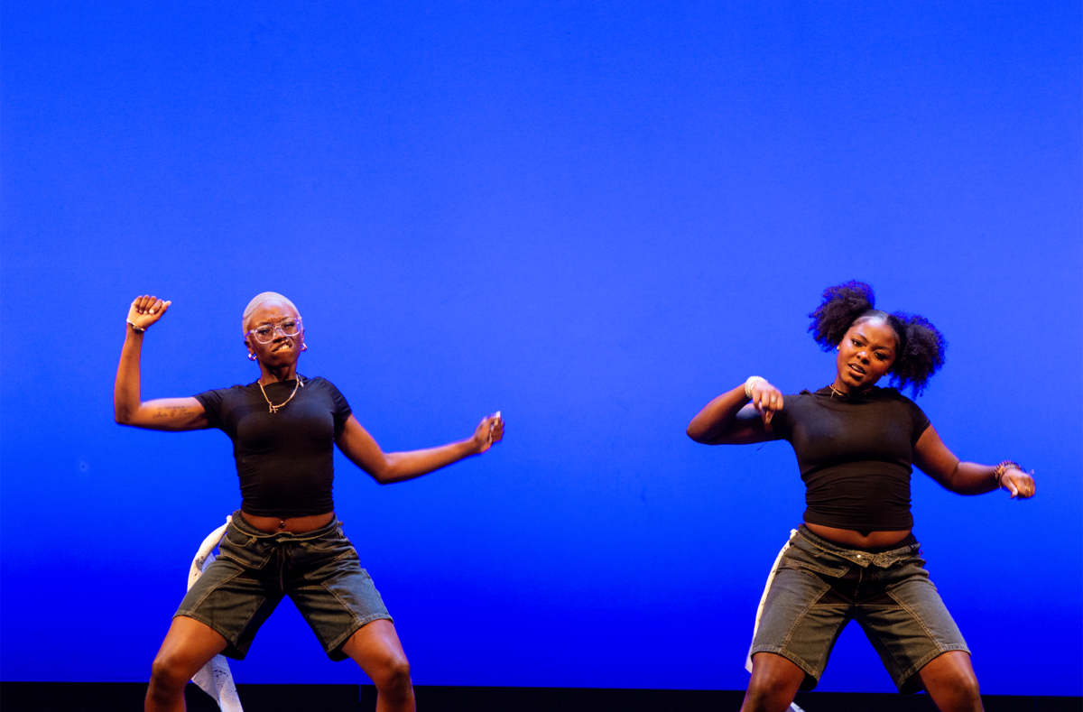 Two NGOMA dancers perform in coordinating black tops and gray shorts in front of a blue background. They were second to compete and left the crowd wanting more with their energy and passion.