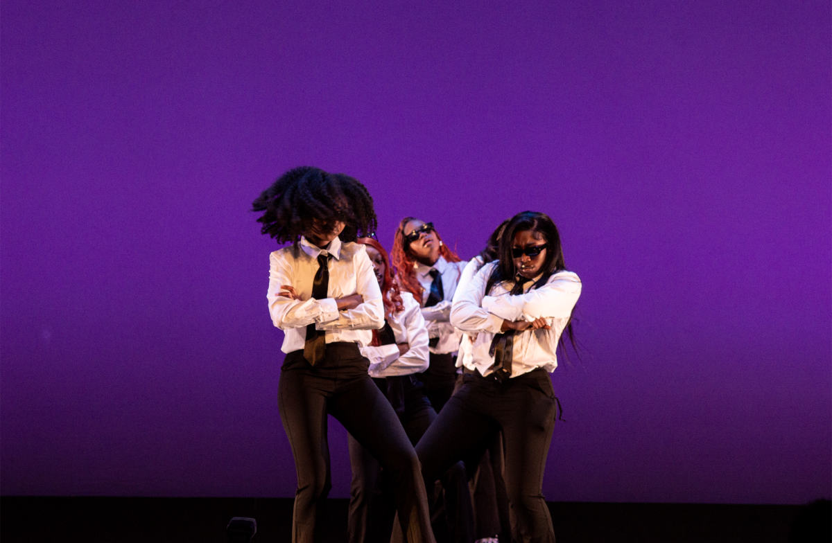 Members of Afrithms perform in white tops, ties, black bottoms and sunglasses in front of a purple background. They were first to perform and made an unforgettable impression on the audience with their synchronized moves, setting the tone for the competition.