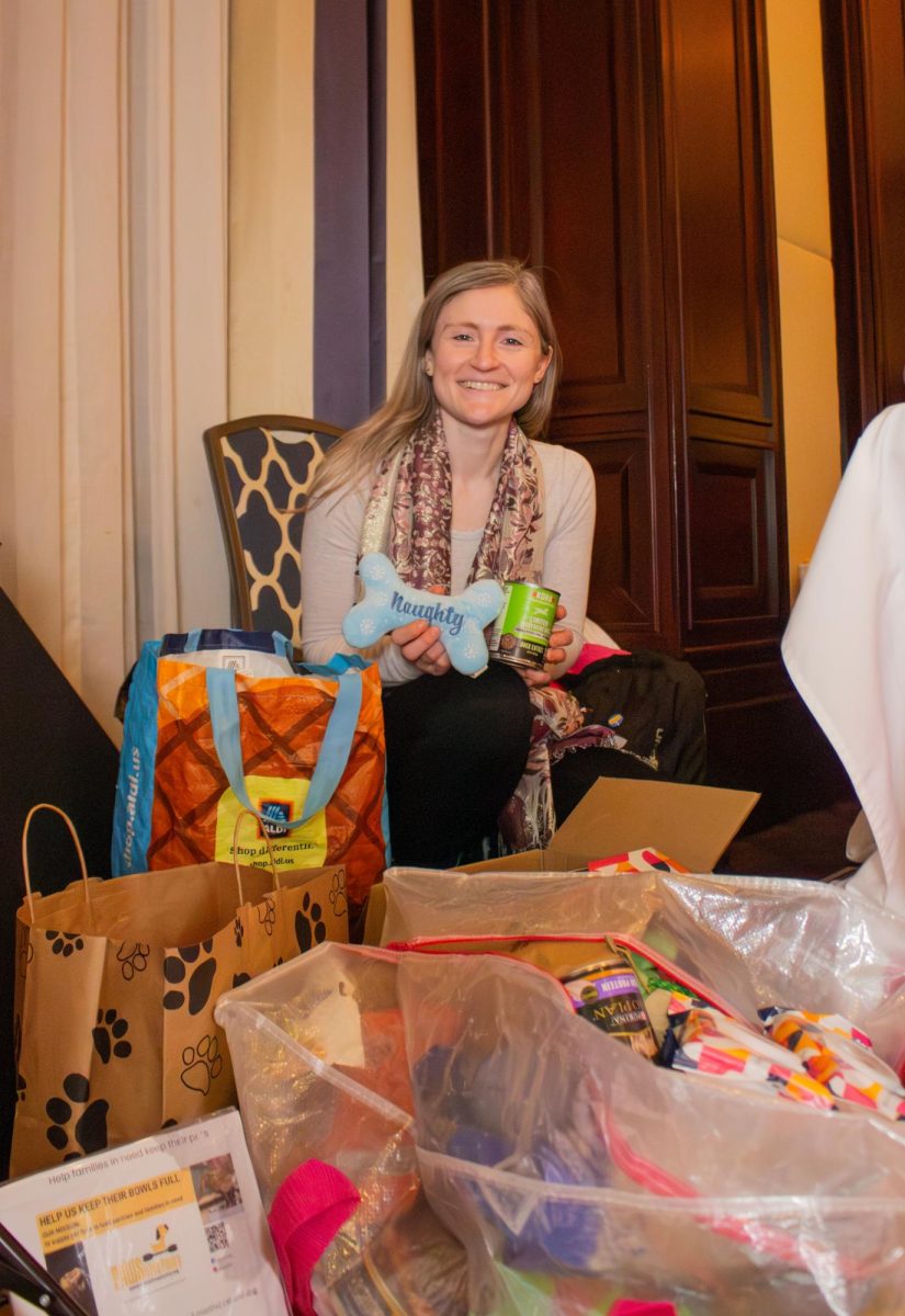 Maggie Gander, A PAWsitive Pantry employee, smiles behind bags of event donations with a dog toy and food can in hand. Participants contributed essential supplies including dog food, toys and pet cleaning wipes.