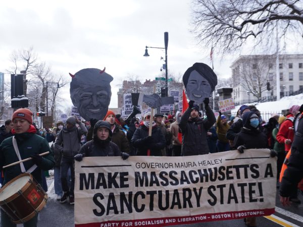 Protesters walk in the street and carry signs depicting  Donald Trump and Maura Healey. Many signs featured anti-ICE rhetoric.