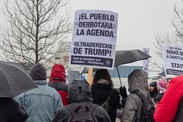 A crowd gathers around a speaker and carries signage. The sign translated to "The people will defeat the agenda, Trump's far right."