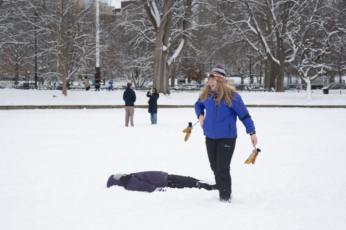 A woman laughs and smiles as her friend lies in the snow beside her on the Public Garden pond. The two took pictures of each other making snow angels.