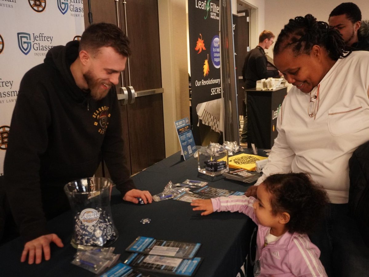 A man running a table advertising a law firm smiles and speaks to a woman and her child. The market section of Winter Wonderland included local artists and businesses.