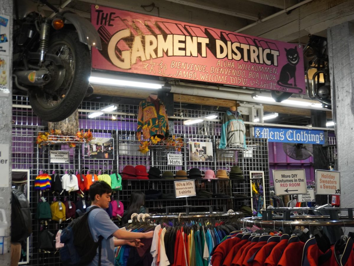 A sign that reads “The Garment District” hangs above a range of hats and clothes.