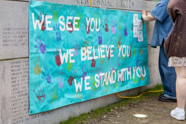 Members of SARC hang a banner on the Centennial Common stone wall. The organization quickly moved the event into Shillman Hall when it began to rain.