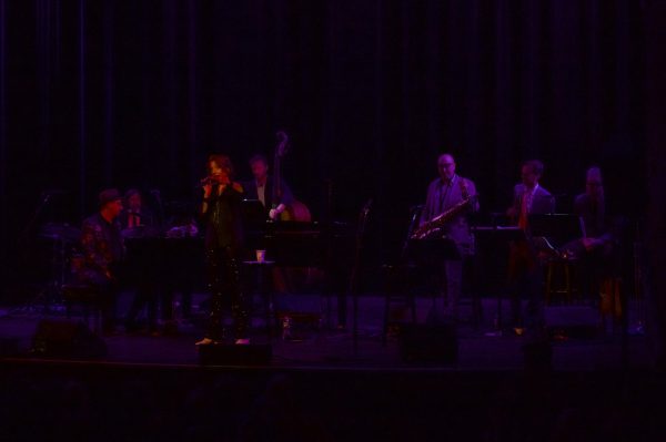 The Hot Sardines sing to an audience in moody lighting. The band used an array of instruments such as a cello, saxophone and piano.