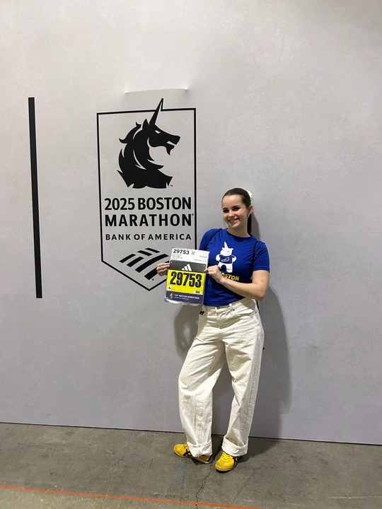 Jen Volk poses in front of a Boston Marathon sign with her bib. The Ed Walsh fund sponsored Volk to run marathon for the nonprofit organization. Photo courtesy Jen Volk.