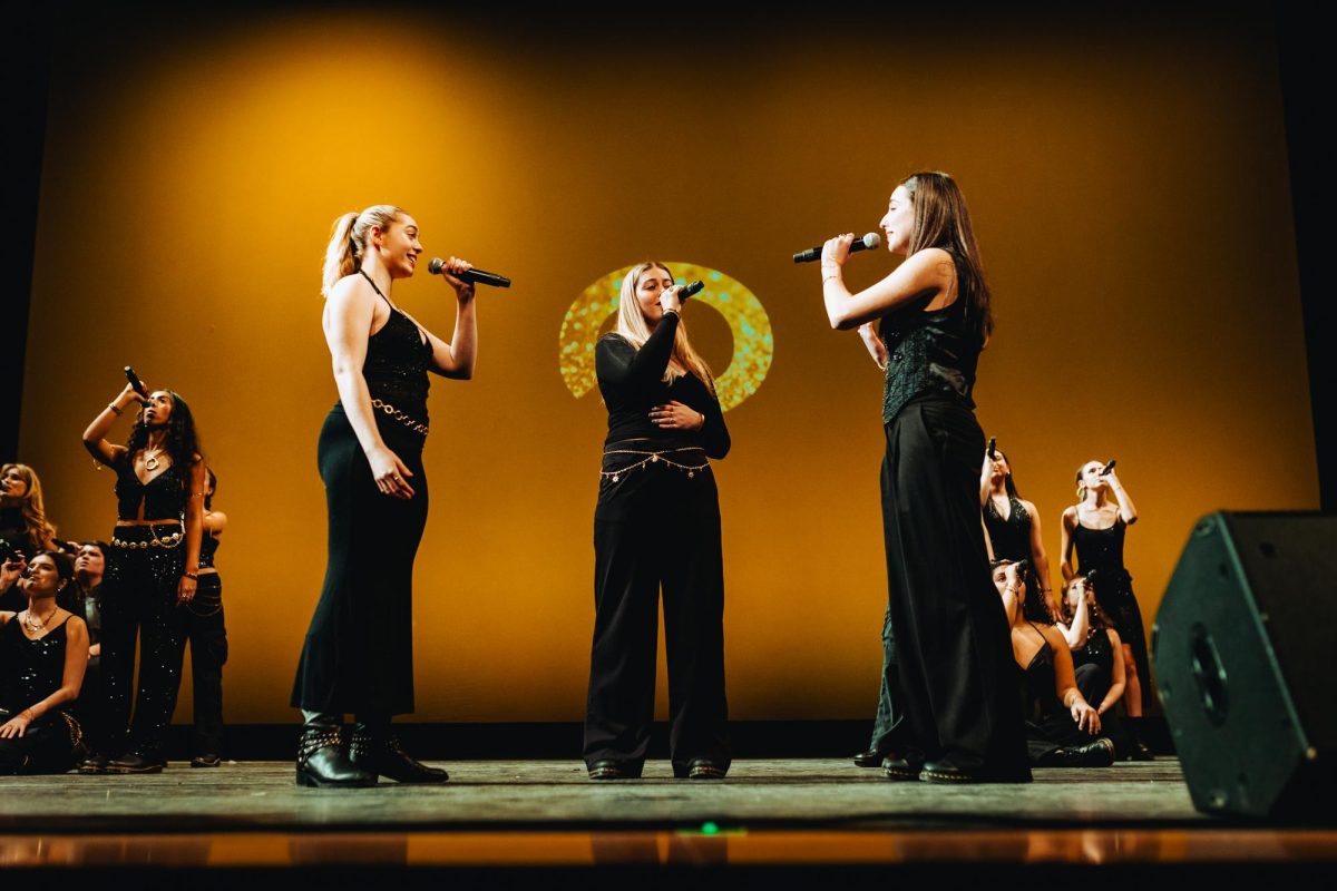 Three Pitch, Please! members sing on a stage Jan. 31. This spring season, the vocal group consisted of 19 a cappella singers, including bass, alto, mezzo and soprano singers. Photo courtesy Pitch, Please!.