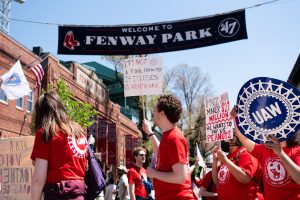 GENU-UAW union members chant and hold signs demanding Northeastern offer better compensation and health care benefits for working graduate students at Fenway Park. The union used the undergraduate commencement as an opportunity to make a statement against the final package proposal the university put forth May 5.