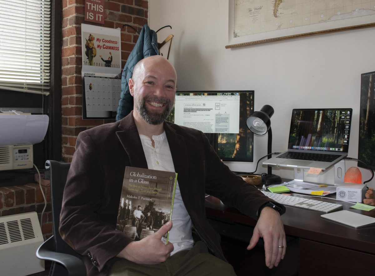 Malcolm Purinton smiles for a picture with his published book in his hands Jan. 22. He formally began studying alcohol while pursuing a master's degree at Northeastern.