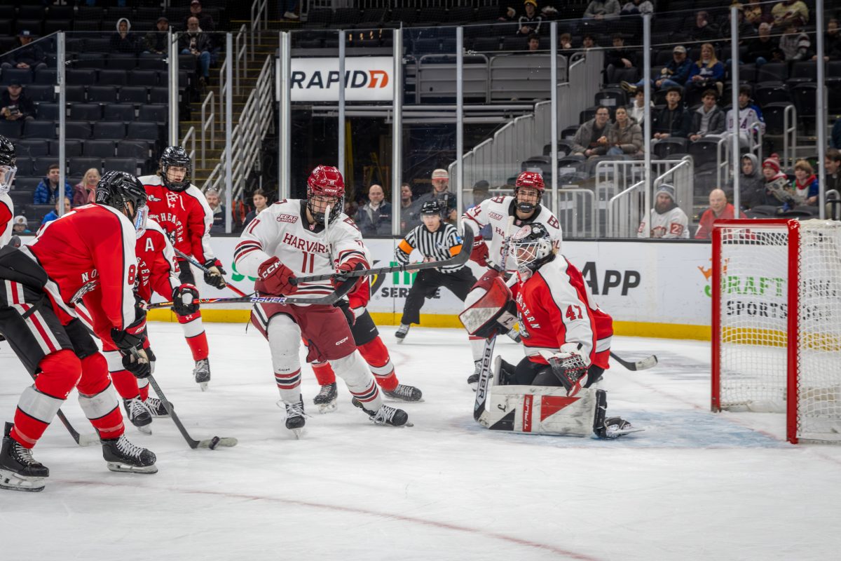 Sophomore forward James Fisher (right) swipes the puck away from Harvard opponents and the goal crease. Northeastern fell to Harvard 4-1 in the Beanpot consolation game Feb. 9.