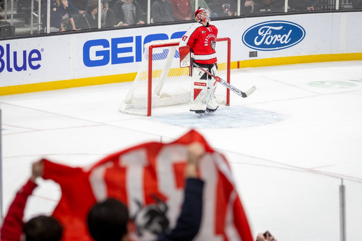 Crowd members raise a Boston University flag, framing a despondent Lawton Zacher. The Huskies fell to the Terriers in shootouts Feb. 2.