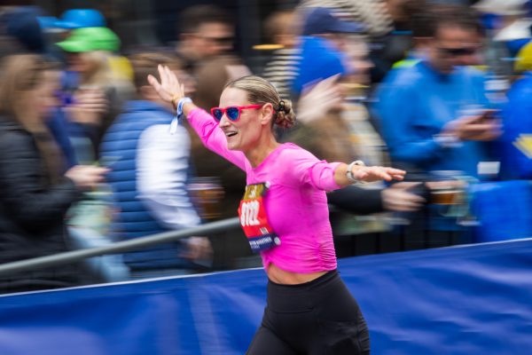A runner spreads her arms and smiles as she passes the Boylston Street cheering section at the finish line. Women made up more than 14,000 entrants in the 2026 race, representing roughly 40 to 45% of the field.